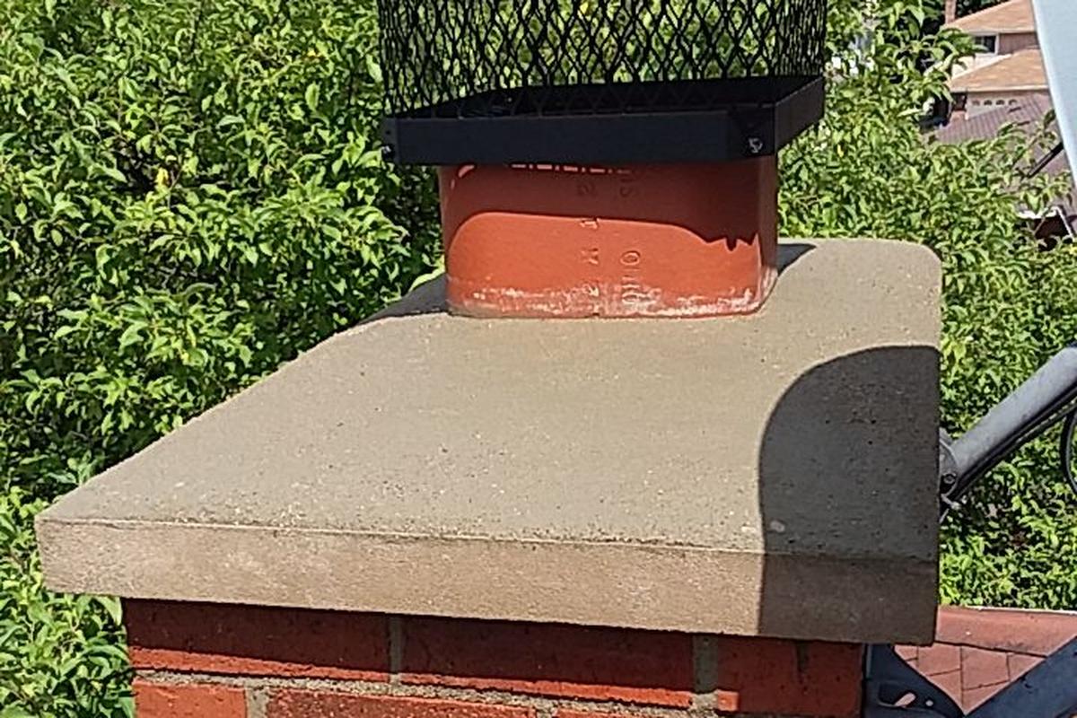 A red brick chimney with a concrete crown and black metal cap, built by WJC Construction