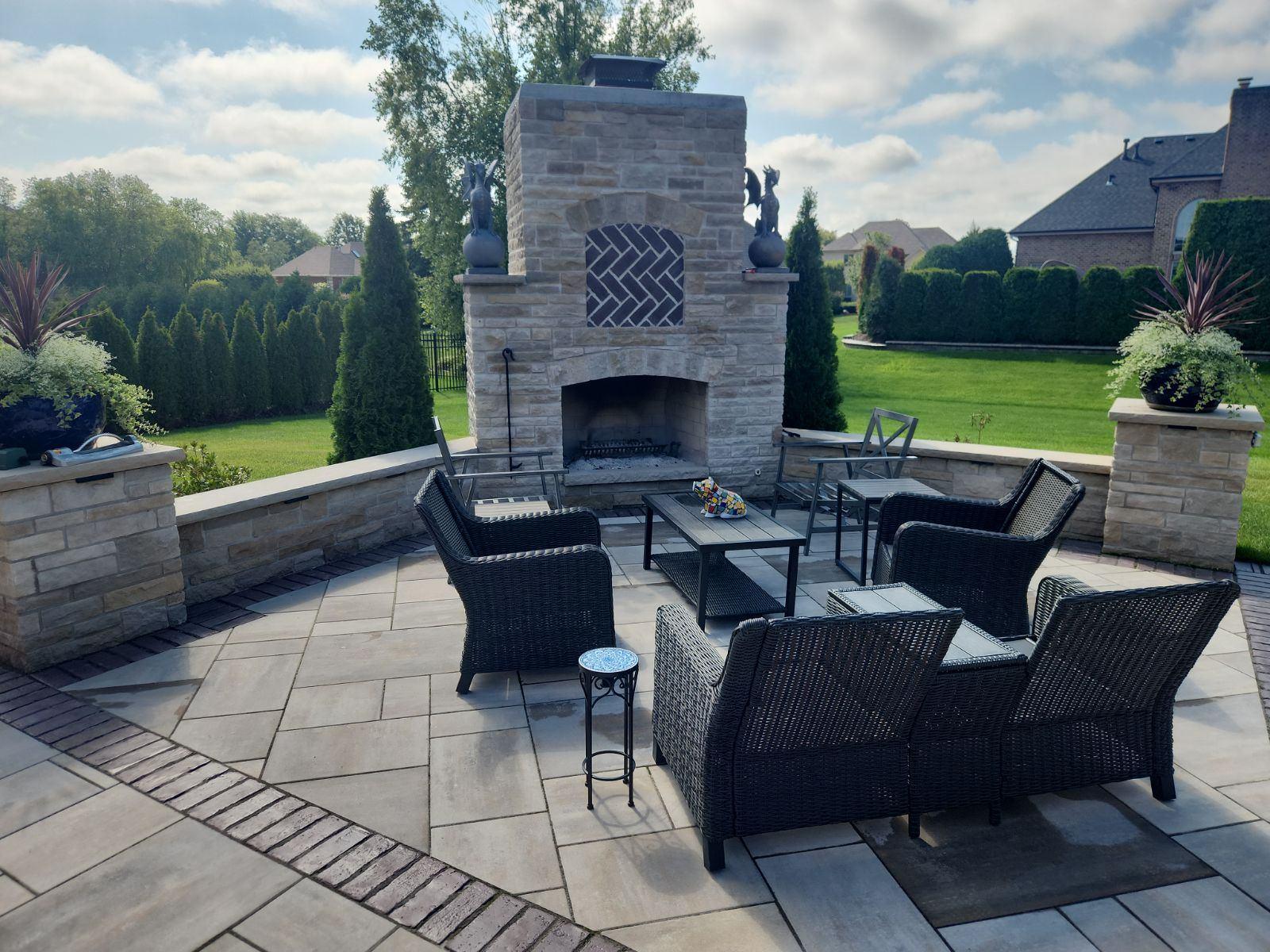 Outdoor fireplace and patio. Stone fireplace with planter pillars and a seat wall around a paver patio.